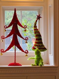 a red christmas tree sitting on top of a window sill next to a green stuffed animal