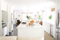 a kitchen with white cabinets and an island in front of the refrigerator, along with two couches