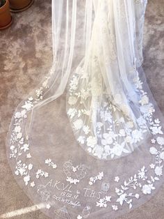 a white veil with flowers on it sitting in front of a potted plant next to a window