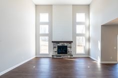 an empty living room with hard wood floors and white walls, windows on either side of the fireplace