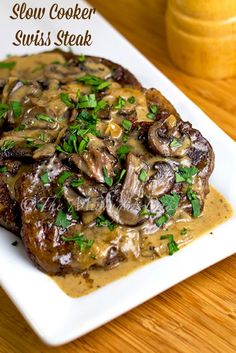 the steak is covered in mushrooms and gravy on top of a white plate