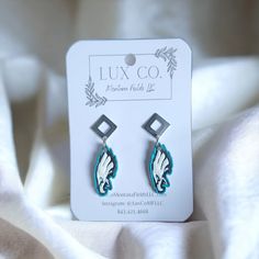 a pair of blue and white earrings sitting on top of a white cloth covered bed