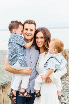 a man and woman are holding two young boys on the beach while they smile at the camera