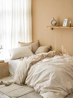 an unmade bed in a bedroom with beige walls and white curtains on the windowsill