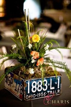 an old license plate planter with flowers and ferns in it sits on a table