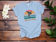 "Show your support for the amazing Karate Moms in your life with this special t-shirt! Perfect for a birthday, holiday, or just because, this fashionable and comfortable t-shirt is a great way to show your appreciation. It features a stylish design with a bold print that reads \"Karate Mom\" - a message of love and admiration for the hardworking moms supporting their athletes. It's also made of a soft and lightweight fabric, making it perfect for any occasion. Whether you're shopping for a speci Fun Blue T-shirt For Gifts, Fun Blue T-shirt For Gift, Blue Screen Print T-shirt As Gift, Fun T-shirt For Mother's Day Gift, Mother's Day Gift Fun T-shirt, Blue Letter Print T-shirt As A Gift, Fun Mother's Day Gift T-shirt, Blue T-shirt For Mother's Day Gift, Blue T-shirt With Text Print As A Gift