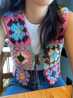 a woman sitting at a table wearing a crocheted vest with flowers on it