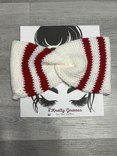 a red and white knitted headband with a bow at the top on a wooden table