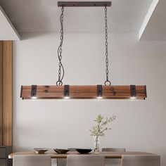 a dining room table and chairs with lights hanging from the ceiling above it, in front of a white wall