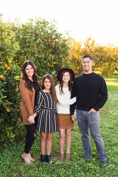 three people standing in front of an orange tree with their arms around each other and smiling at the camera