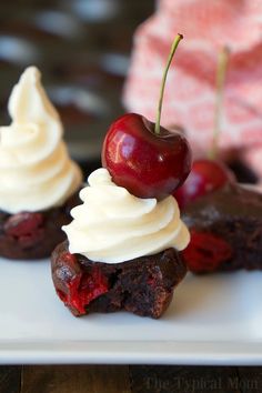 two desserts with cherries and whipped cream on top are sitting on a white plate