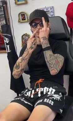 a tattooed man sitting in a chair making the peace sign