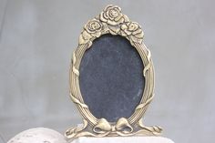 a gold frame with roses on it sitting on top of a white marble block next to a rock