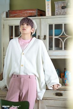 a young man standing in front of a white cabinet wearing pink pants and a cardigan sweater