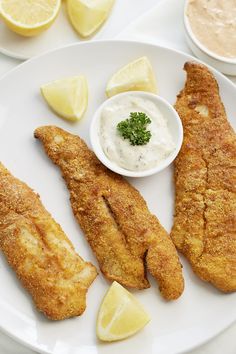 fried fish and dipping sauce on a white plate with lemon wedges next to it