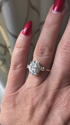 a woman's hand with red nails and a ring on her finger, showing the center stone