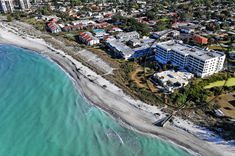 an aerial view of the beach and ocean in front of some buildings with blue water