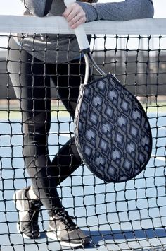 a woman leaning on a tennis net holding a purse