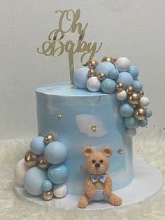 a blue and gold baby shower cake with a teddy bear sitting on the bottom tier