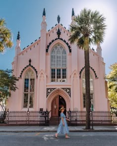 a woman walking in front of a pink church