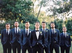 a group of men standing next to each other wearing suits and ties with flowers on their lapels