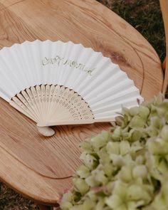 a white fan sitting on top of a wooden table next to a vase with flowers