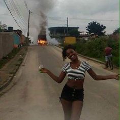 a woman standing on the side of a road holding a beer