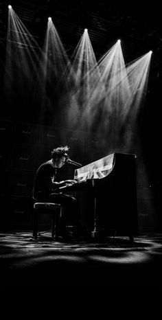 a man sitting at a piano in front of three spotlights on a dark stage