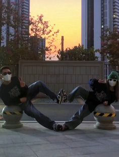 two people sitting on top of cement balls in the middle of a city at sunset