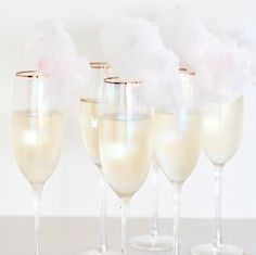 five champagne glasses filled with white wine and cotton floss on a gray tablecloth