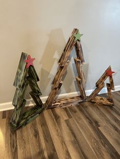 three wooden christmas trees sitting on top of a hard wood floor next to a wall