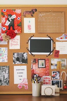 a cork board with pictures and magnets on it next to a cup filled with flowers