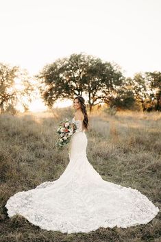 a woman in a wedding dress standing in the middle of a field holding a bouquet