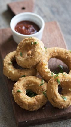 some onion rings on a wooden board with dipping sauce