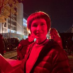 a woman standing in the middle of a street at night with red light on her face