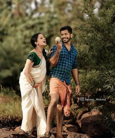 a man and woman standing on rocks in the woods eating something off of a plate