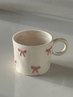 a white cup with pink bows on it sitting on top of a counter next to a window