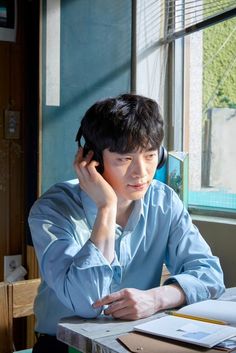 a young man sitting at a table talking on a cell phone and holding his head to his ear