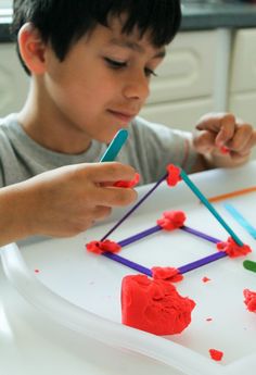 a young boy sitting at a table working on something with colored sticks and plastic shapes