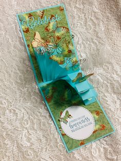 an open card with butterflies on it sitting on a lace tablecloth covered surface next to a tag that says celebrate