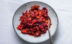 a bowl filled with cranberry sauce on top of a white table next to a spoon