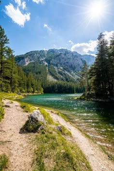 the sun shines brightly over a mountain lake with green grass and trees around it