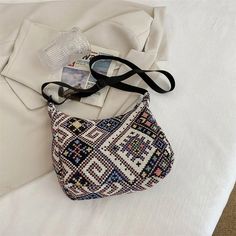 a purse sitting on top of a bed next to a white sheet with a black strap