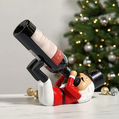 a wine bottle holder with a santa clause figure on it and a christmas tree in the background