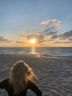 a woman sitting on top of a sandy beach next to the ocean under a cloudy sky