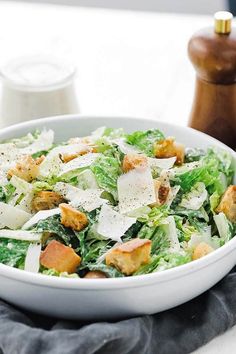 a salad in a white bowl with parmesan cheese and lettuce on top