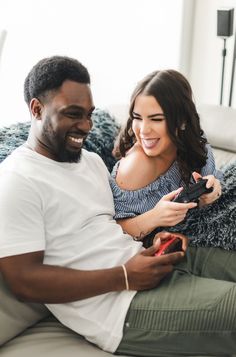 a man and woman sitting on a couch looking at their cell phones while they smile