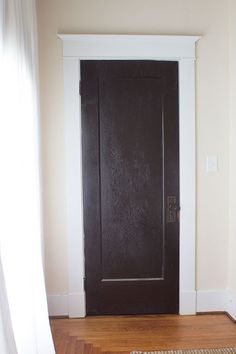 an empty room with a black door and wood flooring on one side, white trim on the other