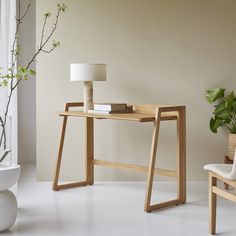 a wooden desk sitting next to a white vase with a plant on top of it