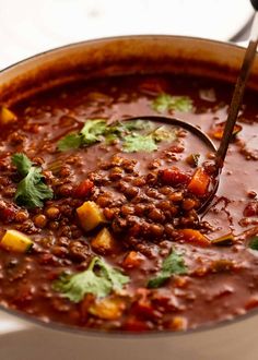 a spoon in a pot filled with chili and other food on top of a table